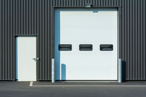 A modern industrial warehouse facade with a large white garage door and side entrance.